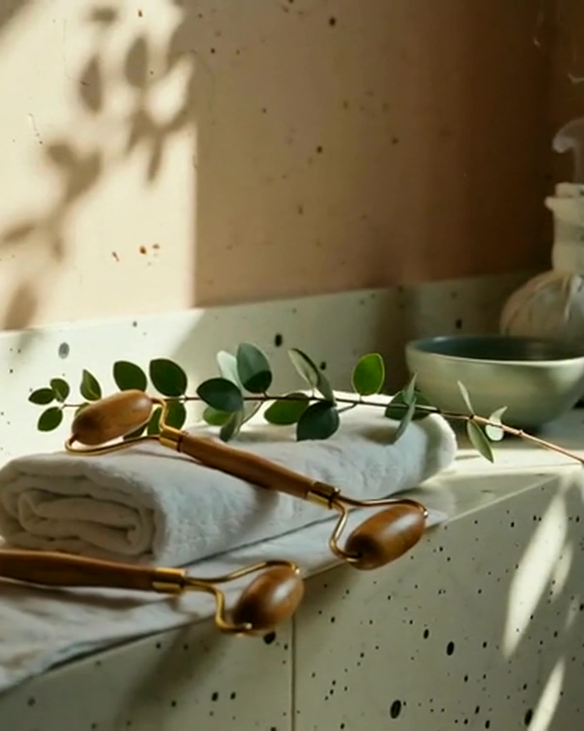 Warm, sunlit still life of wooden massage tools, rolled linen, and eucalyptus